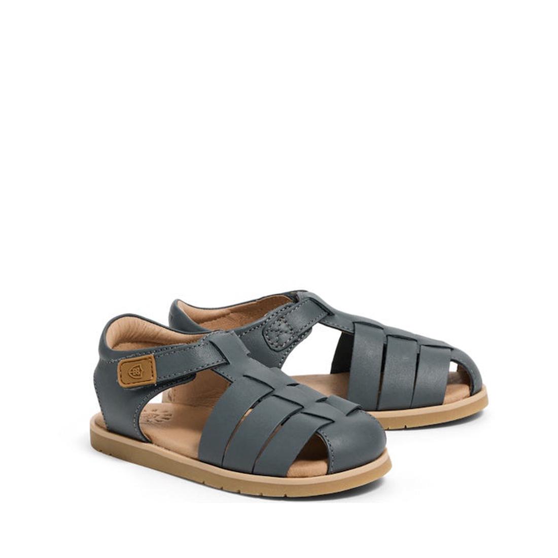 The Pretty Brave Child Rocco Indigo Leather Closed Toe Sandal features a woven indigo leather design, tan sole, closed heel, and adjustable strap with a brown logo patch—perfect breathable summer sandals for kids.