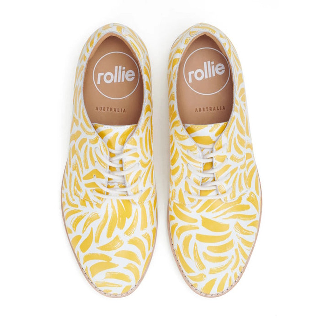 The Rollie Womens Derby Sunshine Splash Leather Shoe offers sneaker-like comfort and features a yellow banana pattern on white. Tan insoles, printed with "rollie" and "AUSTRALIA," are visible from the top view., 9781760774783, 9781760774790, 9781760774806