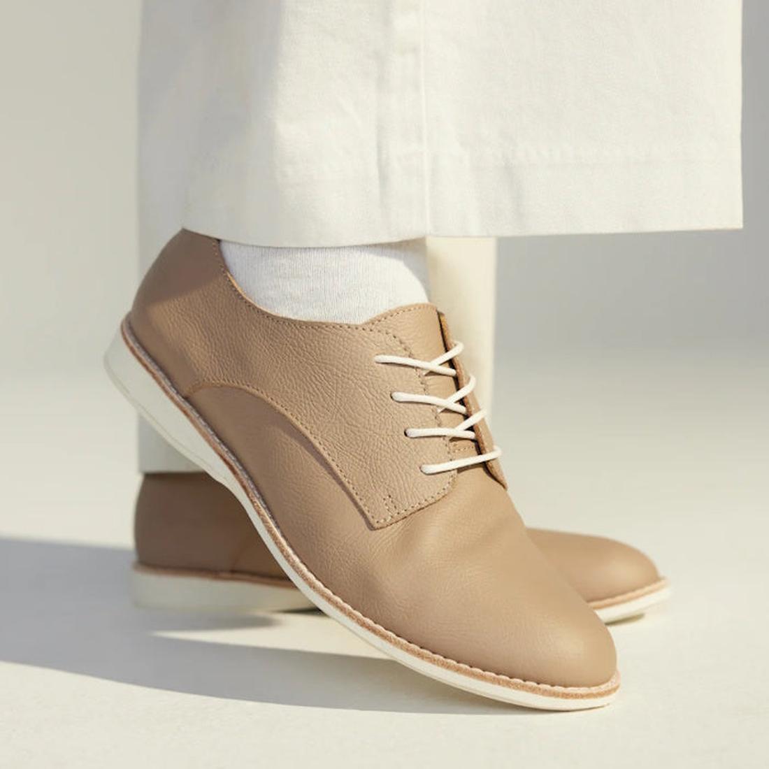 Close-up of a person wearing Rollie Womens Derby Super Soft Clay Leather Shoes in beige, paired with white socks and pants, standing on a light surface with soft lighting., 9781760781552, 9781760781576, 9781760781507, 52452, 52453, 52454