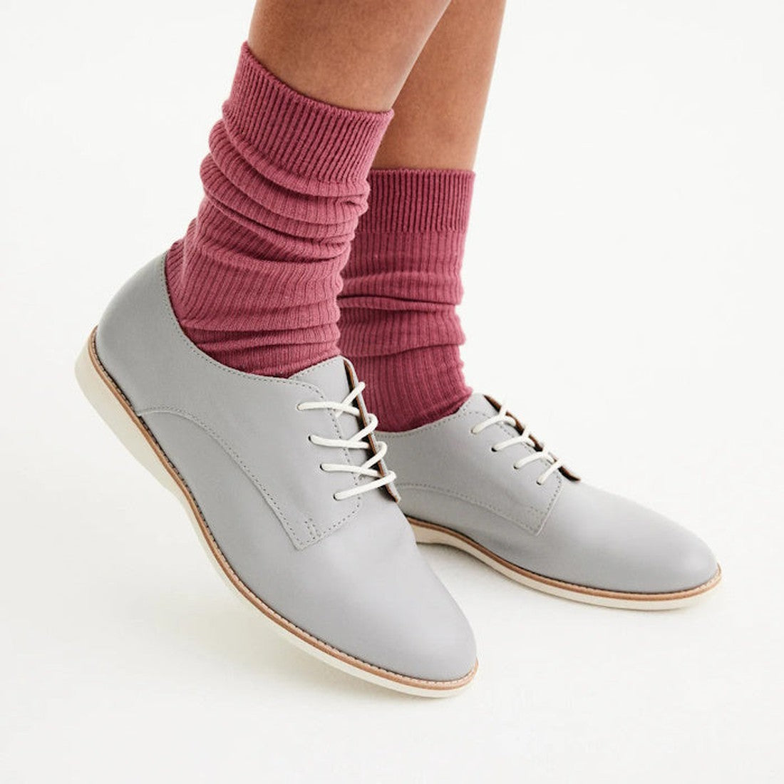 A person wears Rollie Womens Derby Super Soft Stone Leather Shoes and thick, scrunched mauve socks. Only the lower legs and feet are shown against a plain white background., 9781760763930, 9781760763947, 9781760763954, 9781760763961, 9781760763978
