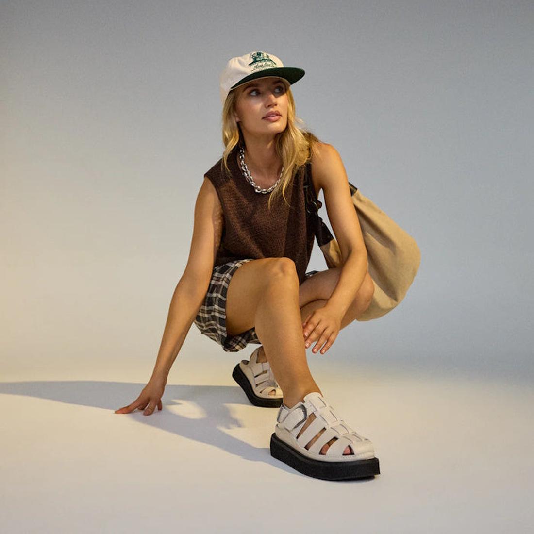 Woman posing on a light gray background wearing a cap, sleeveless top, shorts, and Rollie Hyde Fisherman Sandals in Bone with a black sole.,
9781760788933,
9781760788940,
9781760788957,
9781760788964,
9781760788971,, 9781760788933, 9781760788940, 97817607