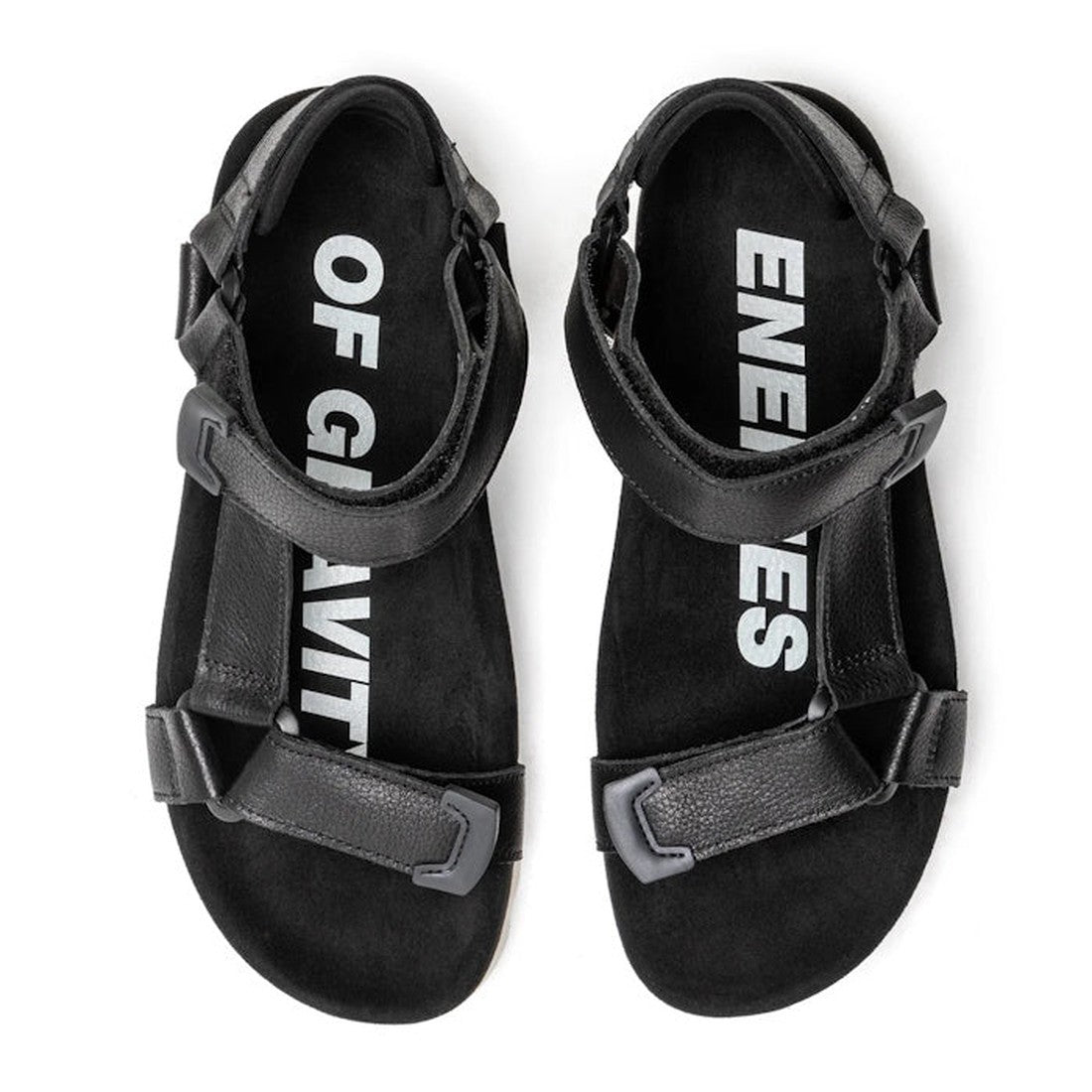 The Rollie Womens Sandal Tooth Wedge Black features adjustable sheep leather straps with velcro closures. Viewed from above, the insoles display white text: "OF GRAVIT" on the left and "ENEMIES" on the right sandal., 9339554310381, 9339554310398, 93395543