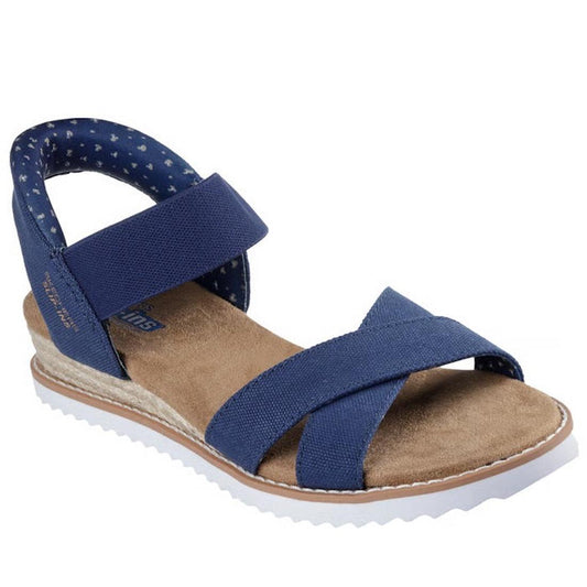 The Skechers Womens Bobs Desert Kiss Golden Lily Navy SLIP IN is a blue vegan slip-on sandal with crisscross fabric toe straps, star-patterned ankle strap, cushioned Memory Foam footbed, and a white ridged outsole.