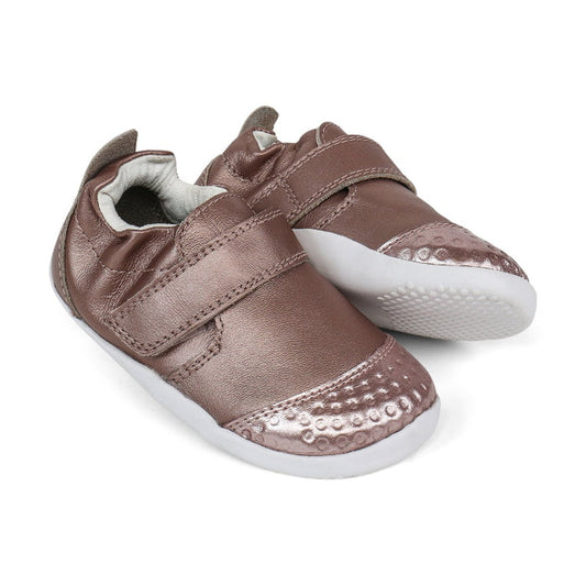 The Bobux Explorer Go Rose Gold First Walker Crawler 501015B features premium soft leather in metallic rose gold, velcro straps, white soles, and textured toe detailing, shown on a white background.
