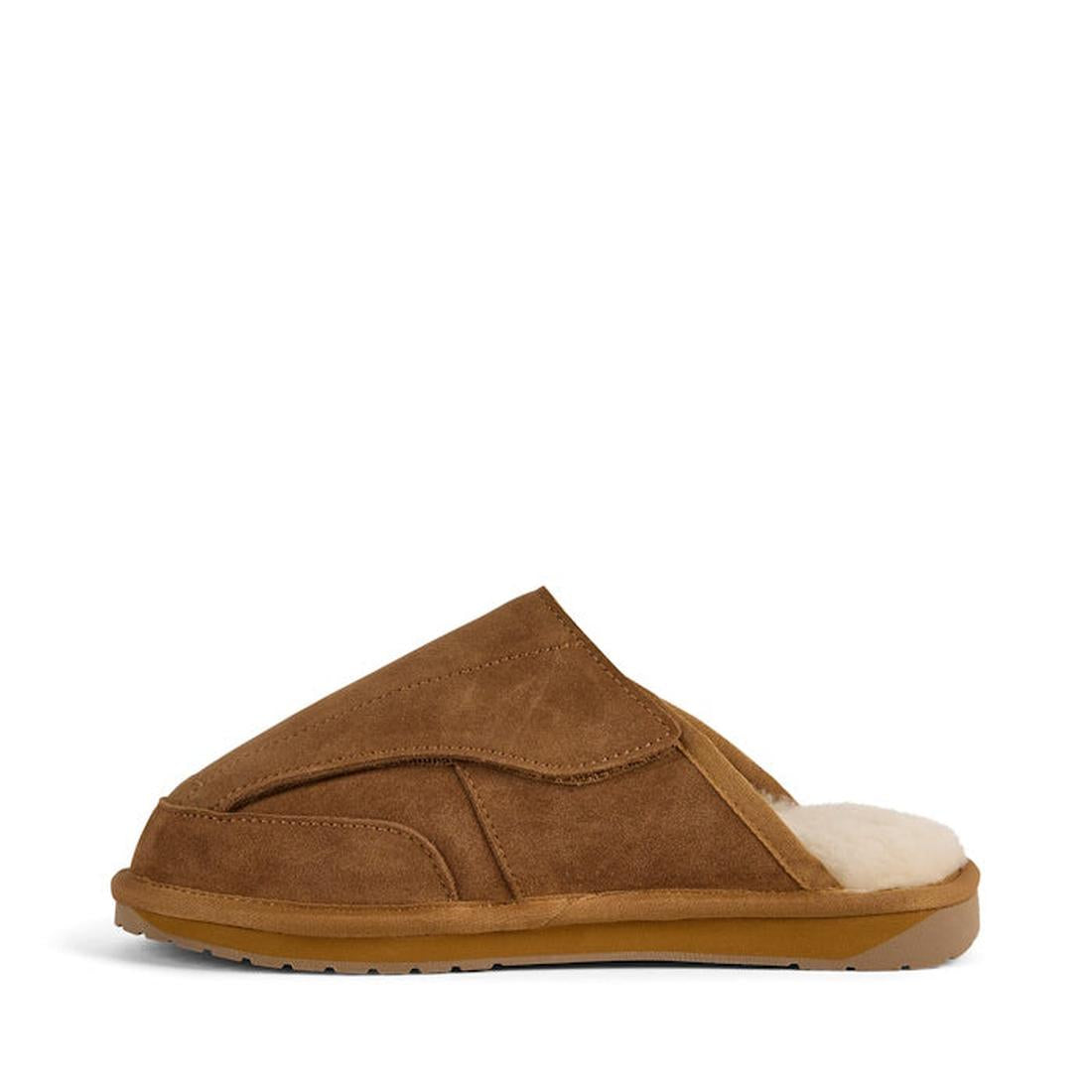 The EMU FlexiCare Wide Opening Sheepskin Scuff Chestnut Slipper features a brown suede exterior, closed toe, open heel, tan rubber sole, and plush off-white lining for warmth and comfort. Shown in side profile on a white background., 9330071991091, 933007