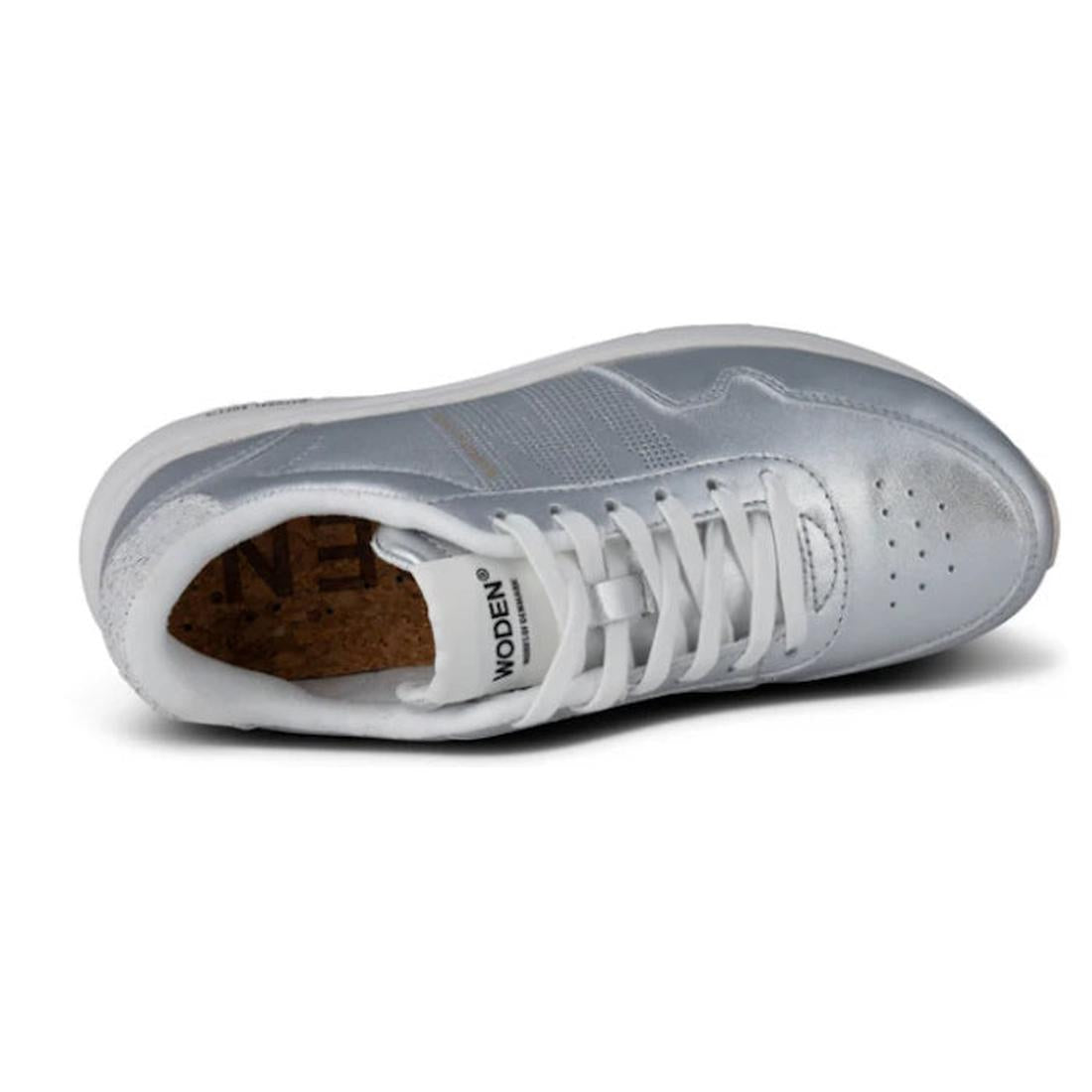 The Woden Womens Sneaker Nora Natural Soft Metallic Silver, shown from above at an angle, features silver and white tones, white laces, a cork insole, perforated toe, visible WODEN branding on the tongue, and upcycled fish leather for sustainability., 424