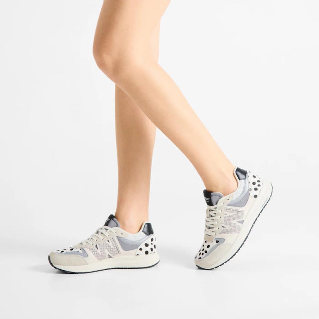 A person wearing Woden Rigmor Animal Damlation Lace Up Sneakers in light gray and white with black accents, made from LWG certified leather, stands on a white background. Only the lower legs and feet are visible., 5713326695267, 5713326695274, 57133266952