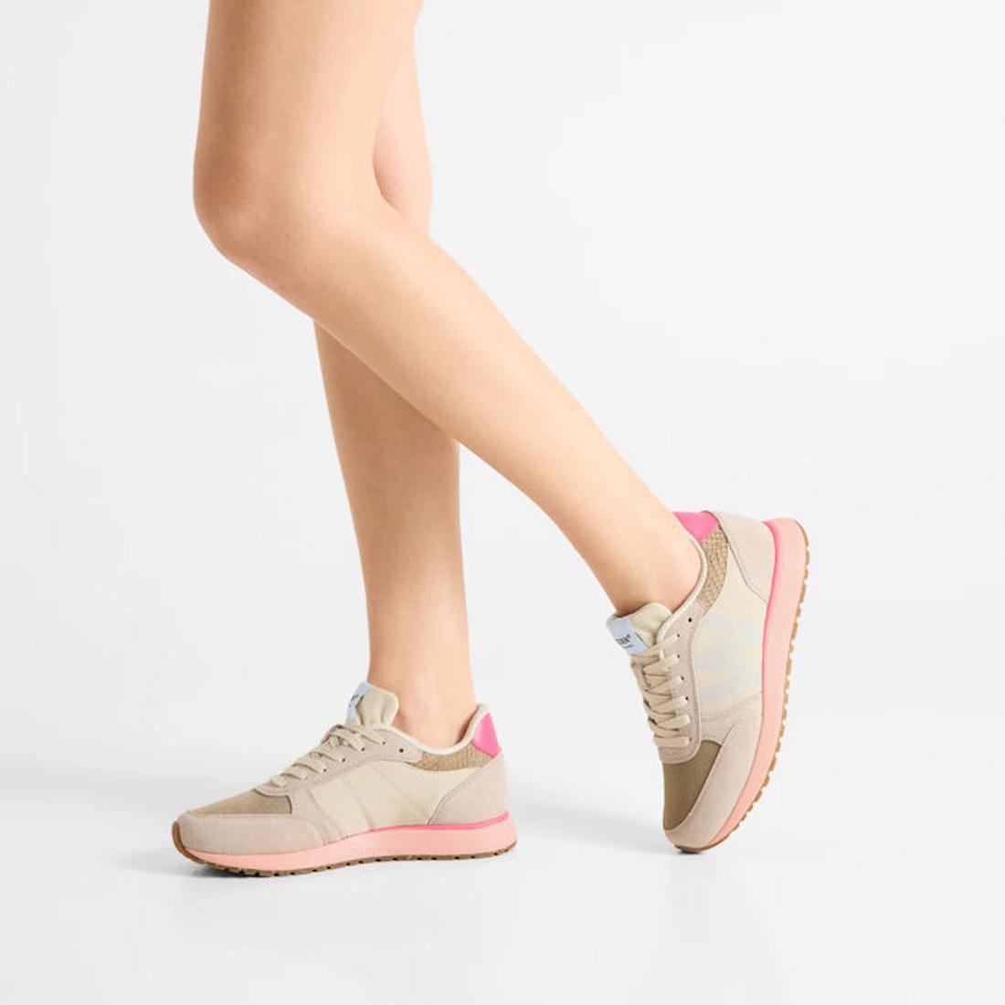 Someone stands on tiptoe against a plain white background, showcasing the side and back of the Woden Ronja Ivory Blush Lace Up Sneaker in beige and pink leather with white soles., 50265, 5713326700633, 5713326700640, 5713326700657, 5713326700664, 57133267