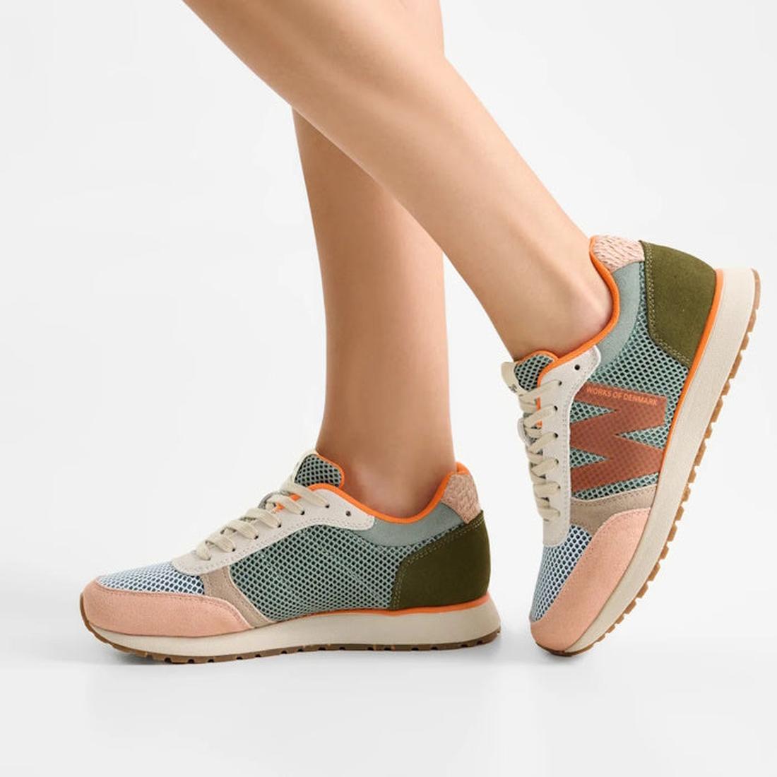 A person wearing Woden Ronja Icon Light Algae Multi Lace Up Sneakers, featuring certified suede, mesh details, and the WODEN Air Flow System in green, pink, and beige, stands on tiptoe against a plain white background., 50275, 5713326699838, 5713326699845