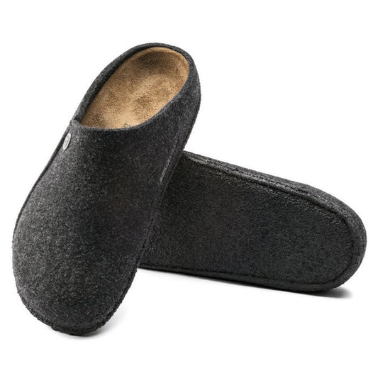 A pair of Birkenstock Zermatt Rivet Felt Anthracite slippers (narrow width, for indoors only) with closed toes, open backs, and a cork latex footbed. One stands upright while the other lies flat underneath, showing their cozy design.