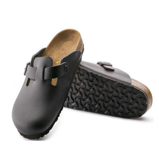 A pair of Birkenstock Boston BS Clog Smooth Leather Regular Black shoes with cork-latex footbeds and textured rubber soles are shown—one upright, the other on its side displaying the wavy tread pattern.