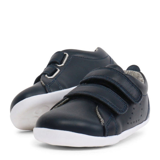 The Bobux Step Up Grass Court Trainer 728915J Navy is a small leather toddler shoe with white soles and double strap closure, ideal as first-walkers shoes, shown on a plain white background.