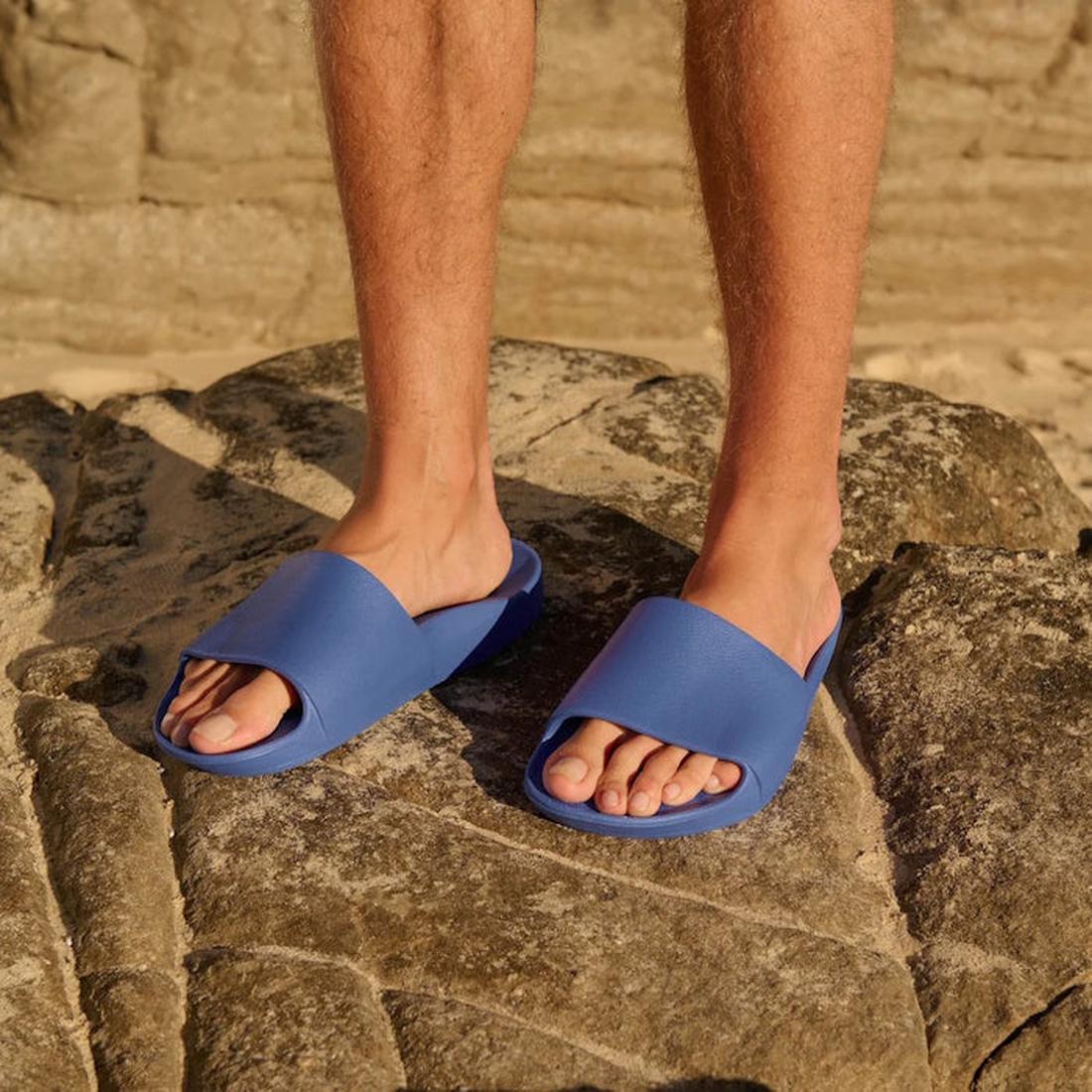An adult wears Archies Footwear Arch Support Slide sandals in Capri Blue, featuring comfy arch support and easy slip-on soles outdoors.  ksnz, 9350311010436, 9350311010443, 9350311010450, 9350311010467, 9350311010474
