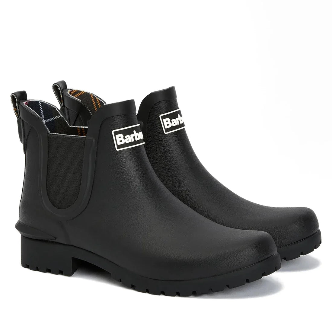 The Barbour Wilton Black Chelsea Wellingtons Womens Rainboot features elastic sides, pull tabs, rugged soles, and a tartan lining, shown against a white background.