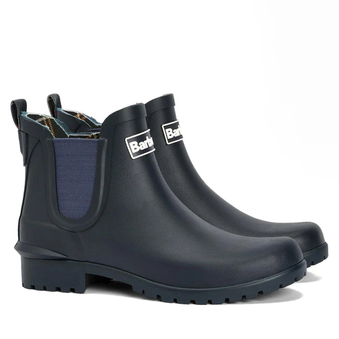 The Barbour Wilton Navy Chelsea Wellingtons Womens Rainboot features dark blue ankle height, chunky soles, tartan lining, side panels, pull tabs, and the Barbour logo on the front.