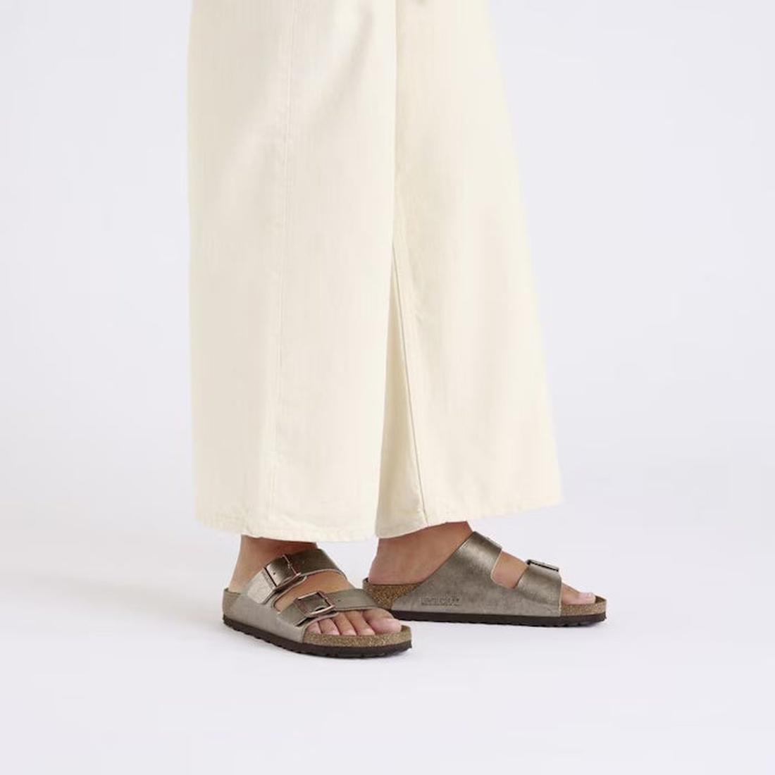 Person wearing Birkenstock arizona graceful taupe metallic sandals with light-colored pants on a white background.,
4067707034901,
4067707034949,
4067707034987,, 45104, 45105, 4067707034864, 4067707034901, 4067707034949, 4067707034987, 45110, 45111