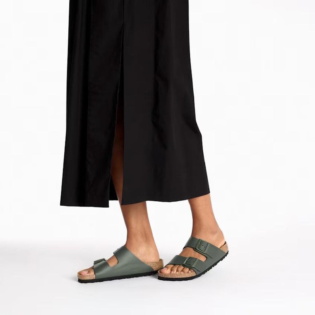 A person wearing a long black skirt and Birkenstock Arizona Smooth Leather Thyme Regular Width sandals with adjustable two-straps and cork soles stands against a plain white background., 45282, 45283, 45284, 4066648927563, 4066648927600, 4066648927648, 40
