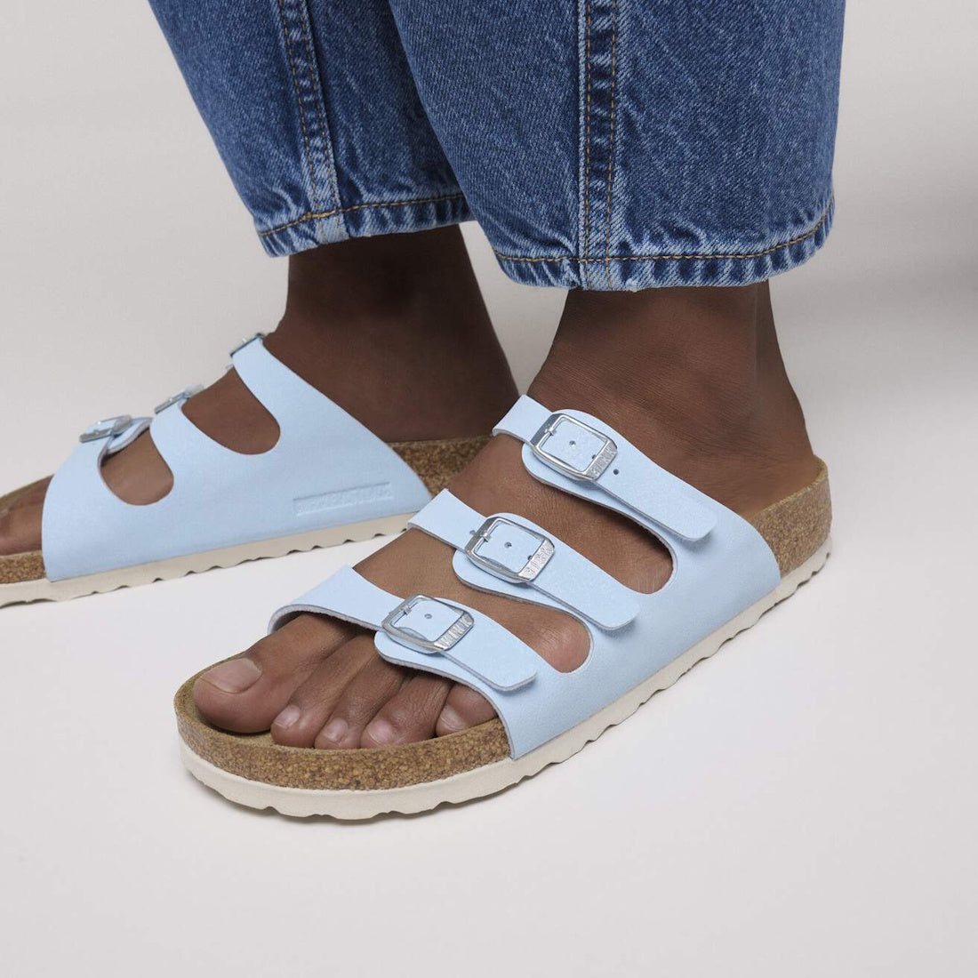A person wearing Birkenstock Florida Finished Sky Blue Birkibuc sandals (regular width) with silver buckles and cork soles, paired with blue denim jeans., 48724, 4067707274567, 4067707274604, 4067707274642, 4067707274680, 4067707274727