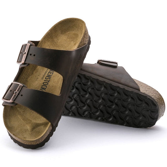 a pair of Birkenstock Arizona Oiled Leather Leather Habana Brown Narrow Width with double straps, one over the foot and one over the toes with buckle adjustment. Staps are linked at the sides of the foot. Leather thick straps and a suede leather footbed,