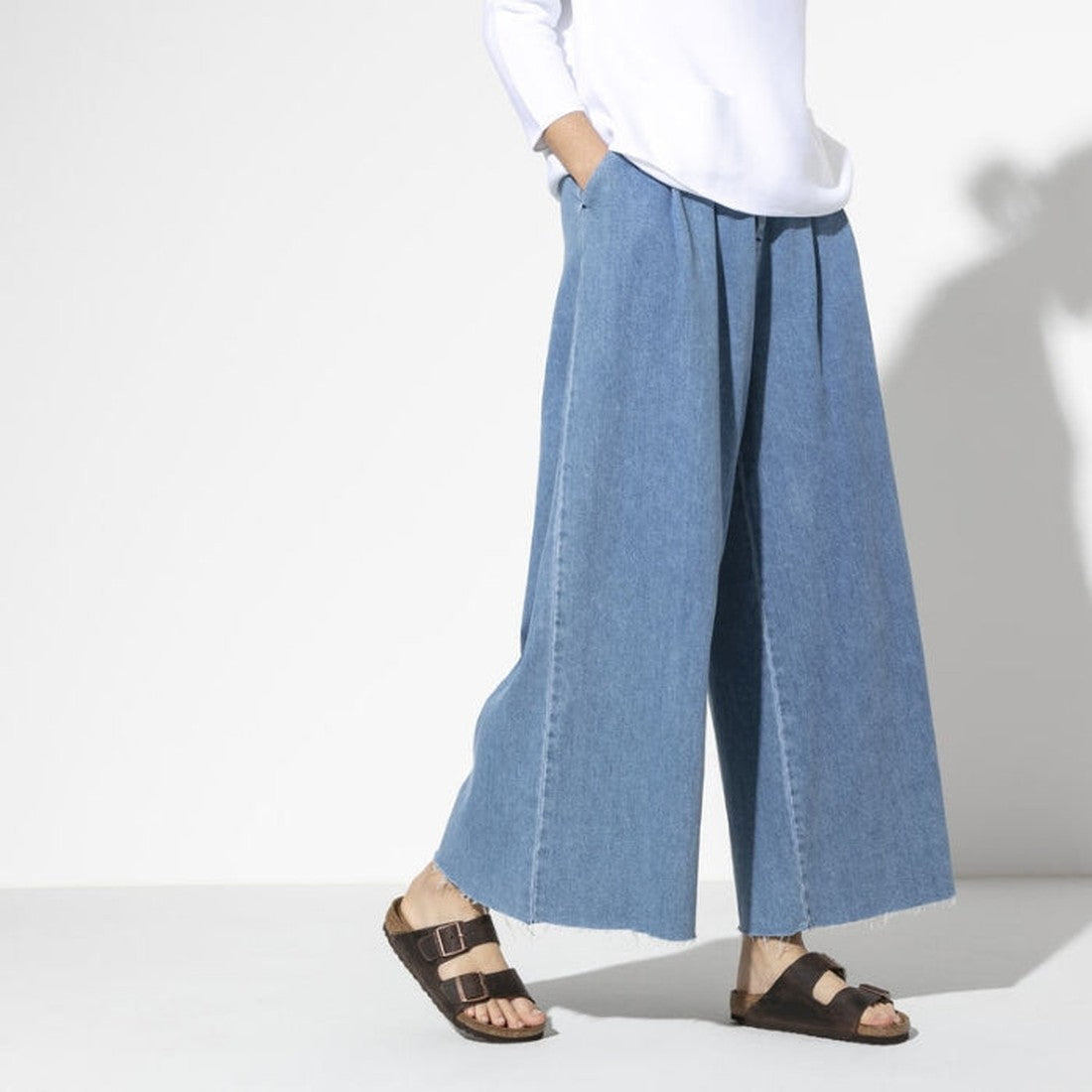 A shot of a models legs & feet weraing light blue denium wide leg jeans with Birkenstocks Habana Arizona Slide in narrow width. Shows both feet the outer side of the right foot and inner side of the left foot. Showing the 2 straps and buckle detailing.,
4