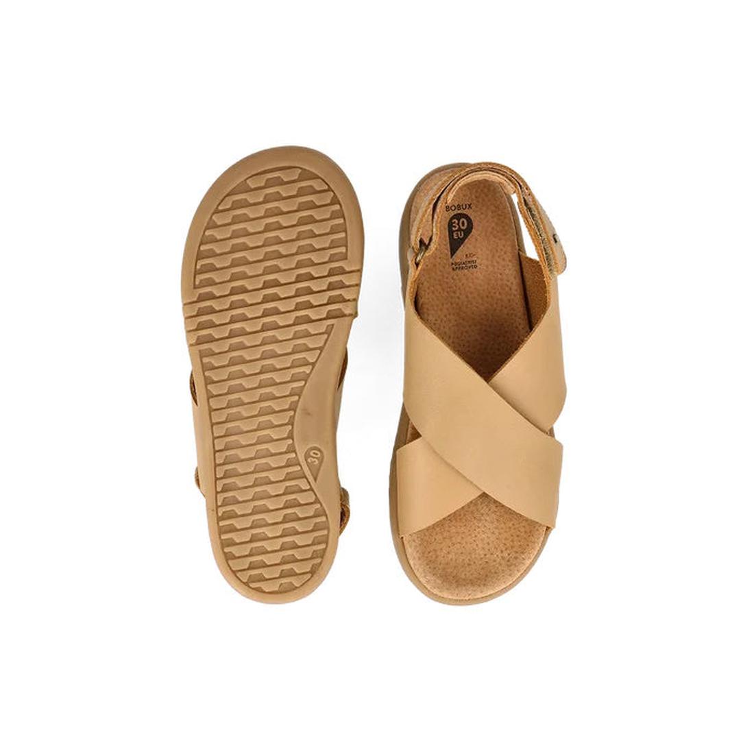 The Bobux Kid+ Plus Glide Parchment Beige Open Toe Sandal for kids features tan leather with crisscross straps, an adjustable heel strap, and a textured rubber sole; one sandal is shown from the top and the other from the bottom., 9420075773110, 942007577