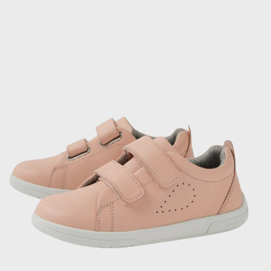 The Bobux KP Kids Plus Grass Court 2 II Leather Sneaker in Seashell is a light pink kids' leather shoe with white soles, two adjustable velcro straps, and side perforations for ventilation, shown on a plain white background.