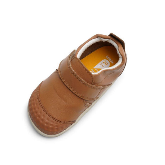 The Bobux Xplorer Go Caramel Tan First Walker 501037 is a single soft leather brown shoe with a velcro strap, textured toe, yellow insole, and flexible sole, shown from above on a white background.