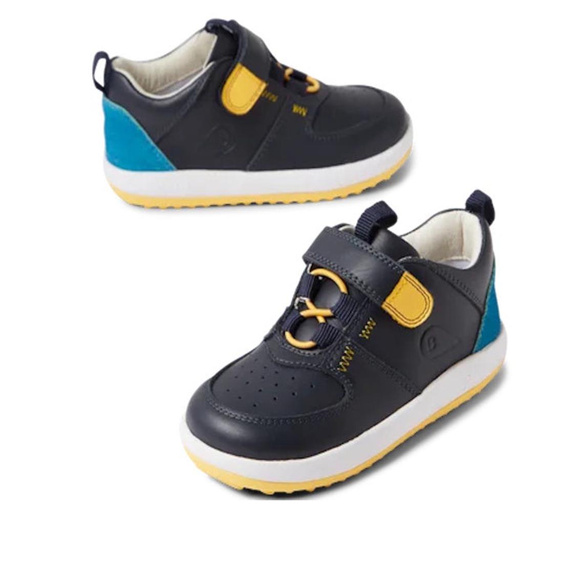The Bobux Kid+ BackSpin Leather Mid Boot Sneaker 853002 Navy features dark blue leather uppers, yellow and blue accents, a lightweight EVA midsole, white soles, and a velcro strap. Displayed on a white background.