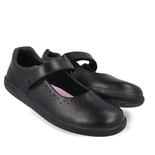 The Bobux Kid+ Bestie Mary Jane Black School Leather Shoe is a kids’ leather school shoe with a classic Mary Jane design, velcro straps, and small perforations on the upper, shown against a white background.