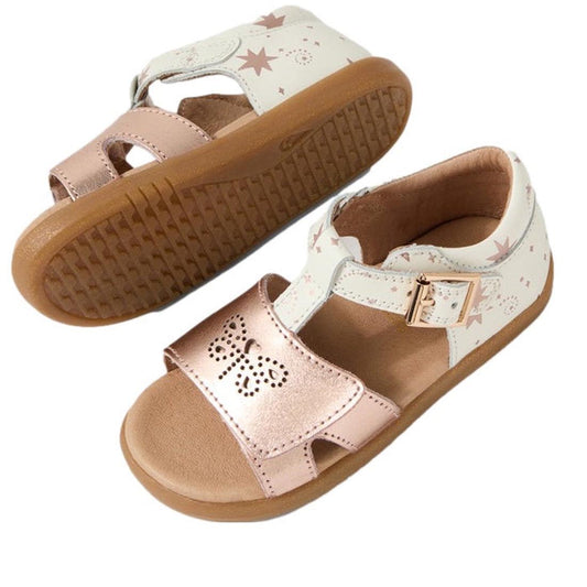Bobux IW Iwalk Haven White Rose Gold Open Toe Sandals for kids have tan rubber flexible soles, white and metallic pink straps, an adjustable buckle, a butterfly cutout on the front strap, and star patterns on the ankle strap.