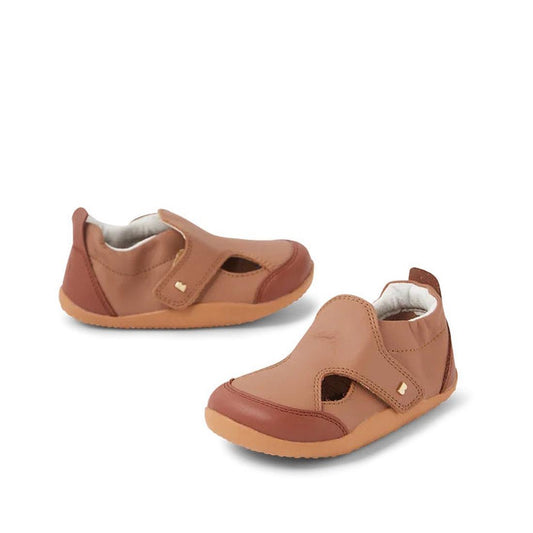 The Bobux XP Explorer Breeze First Walker Sandal Brown 502407 features brown closed toes, tan flexible soles, hook-and-loop straps, a soft design, and gold square accents on the straps—perfect for toddlers.