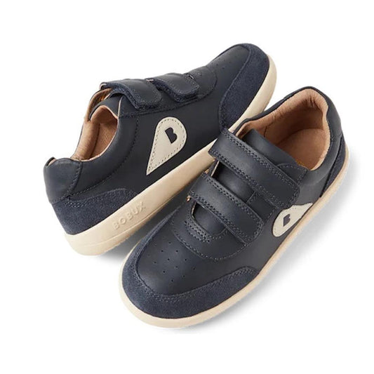 The Bobux Toddlers IWalk IW Champ Sneaker Navy 650509 features navy leather, beige soles and side accents, two hook-and-loop straps, perforated toe details, and the BOBUX logo on the heel.