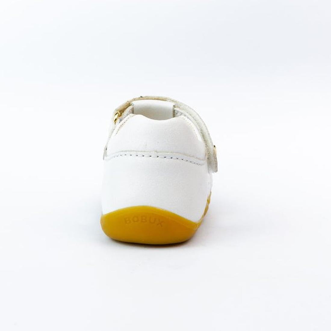 A Bobux Step Ups Cross Jump White 731106 closed toe sandal for first walkers, shown from the back on a white background. It features a white leather upper, yellow sole, and BOBUX embossed on the heel., 9420062083901, 9420062083918, 9420062083925, 94200620
