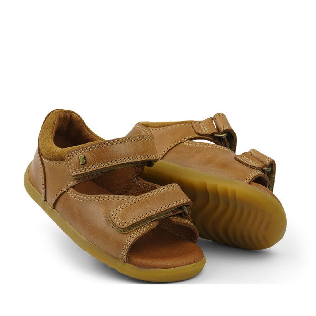 The Bobux Step Up - Driftwood 728609A Caramel Tan are brown leather baby sandals with velcro straps and yellow rubber soles, shown on a white background—perfect first walkers for little feet.