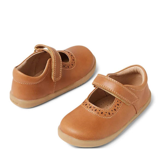 The Bobux Iwalk Lola Toddlers Mary Jane 652801 are caramel tan leather kids' shoes with a flexible sole, toe perforations, and a hook-and-loop strap, shown on a white background.