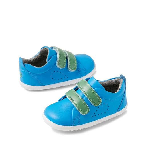The Bobux Step Up Grass Court Trainer Brilliant Blue 734212 toddler shoes feature a leather upper, white soles, and green Velcro straps, shown on a white background.