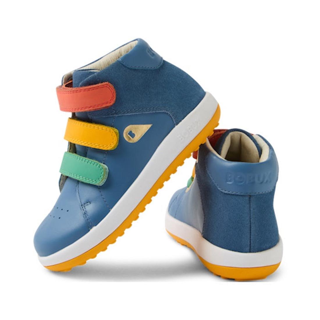 A pair of Bobux IW Iwalk Gamepoint Leather Boot Coronet Blue kids’ sneakers feature blue leather, orange anti-slip rubber soles, and three velcro straps in red, yellow, and green. One shoe stands upright; the other is tilted to reveal the back.