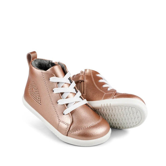 A pair of shiny IWalk IW Bobux Alley Oop Boot Leather Toddlers in Rose Gold Metallic, styled as high-top sneakers with white soles and laces; one stands upright, the other lies on its side, showing the textured sole.