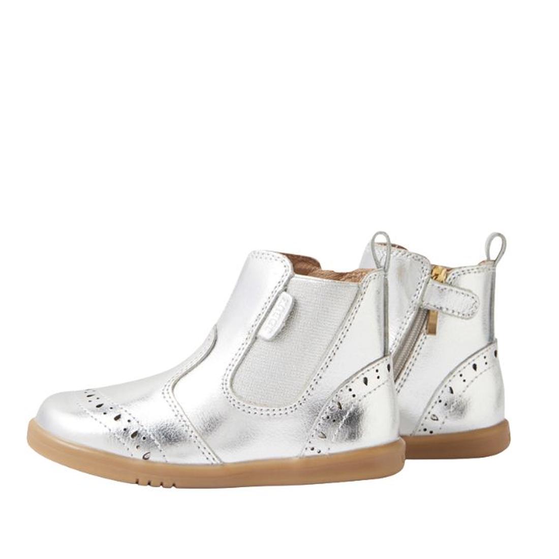 The Bobux IW Iwalk Billie Jodhpur Girls Leather Boot in silver features shiny leather, flexible soles, side zippers, elastic panels, and decorative perforations. One boot is shown facing forward; the other displays its side profile., 9420074856302, 942007