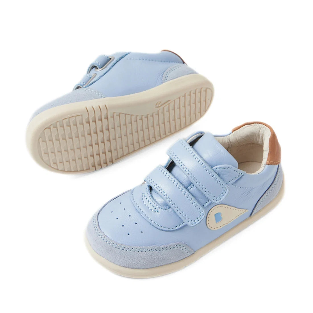 A pair of Bobux IW Iwalk Toddlers Champ Leather Sneaker Skyway Blue displayed from a side and bottom angle on a white background, featuring light blue leather uppers, beige soles, convenient hook-and-loop straps, and a small brown accent on the heel., 942