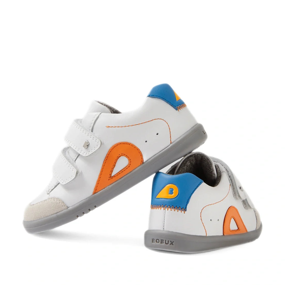 Two Bobux IW Iwalk Blaze Toddlers Leather Sneakers in White Orange, featuring gray soles, orange and yellow side accents, blue heel tabs, and Velcro straps. Crafted from quick-drying leather, one sneaker stands upright while the other is tilted to display