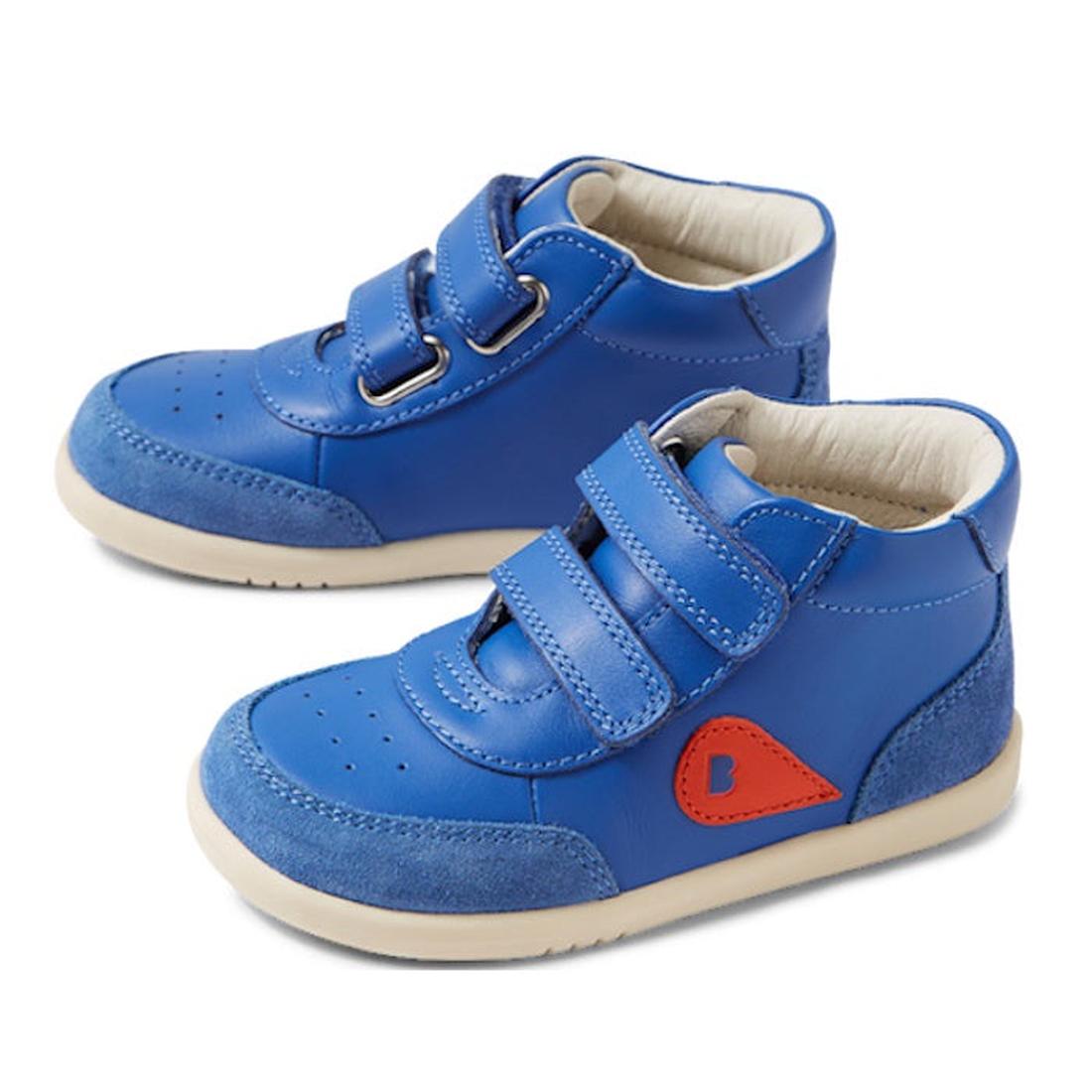 The Bobux IW Iwalk Champ Hi Boot Olympian Blue is a toddler sneaker with Velcro straps, white soles, a red "B" patch on the side, and suede toe and heel accents for added style and comfort.