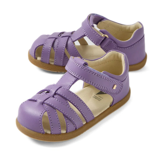 The Bobux Iwalk IW Cross Jump Toddlers Purple Haze Leather Sandals feature closed toes, tan soles, and adjustable velcro ankle straps, providing comfort and support for kids during all-day play.