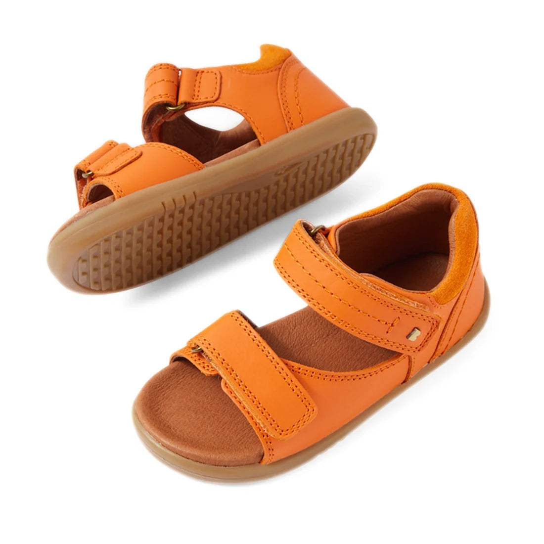 Two Bobux IWalk Driftwood Sandal Orange Peel open-toe leather sandals for toddler boys are displayed: one upright and the other on its side to showcase the light brown, textured rubber sole. These sandals feature adjustable Velcro straps and are designed 