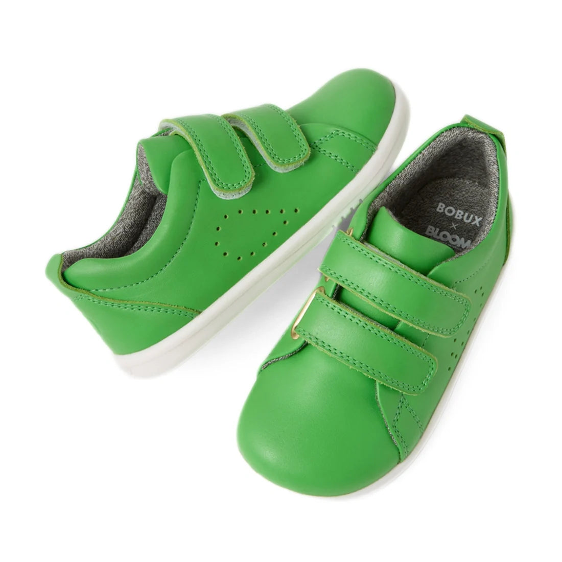 Two green Bobux Iwalk Toddlers Grass Court Retro leather trainers with white soles and double Velcro straps. One shoe stands upright while the other is angled, revealing a grey inner lining and the “Bobux Grass Court” branding printed inside.
