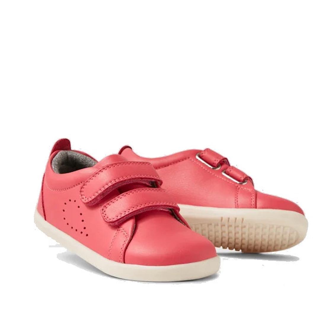 Two Bobux IW Iwalk Grass Court Leather Sneakers in Radiant Raspberry for toddlers are shown. One upright sneaker displays Velcro straps; the other lies on its side, highlighting the textured white sole.