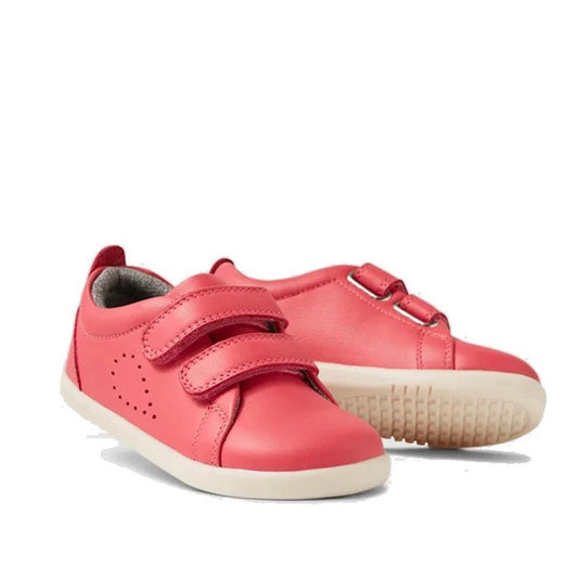Two Bobux IW Iwalk Grass Court Leather Sneakers in Radiant Raspberry for toddlers are shown. One upright sneaker displays Velcro straps; the other lies on its side, highlighting the textured white sole.
