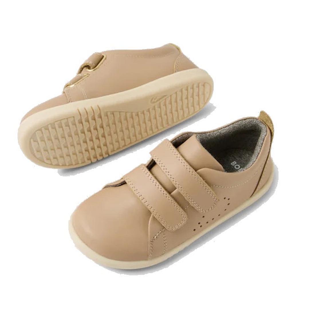 The Bobux IW Iwalk Grass Court Leather Sneaker in Warm Taupe features a premium leather upper, rounded toes, rubber soles, and two Velcro straps. One shoe is shown upright from the top and side; the other highlights the textured sole., 9420074803368, 9420