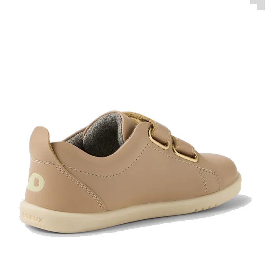 The Bobux IW Iwalk Grass Court Leather Sneaker in Warm Taupe is a light brown toddler shoe with a premium leather upper, two Velcro straps, beige sole, and visible stitching—shown from back and side on white. Perfect for street-styled collections., 942007