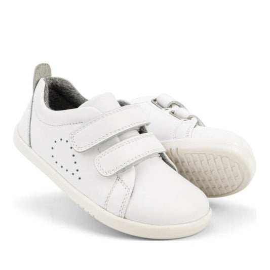 The Bobux Iwalk Grass Court Sneaker Optical White 640510 is a pair of kids' white leather sneakers with double velcro straps and side perforations, shown on a white background.